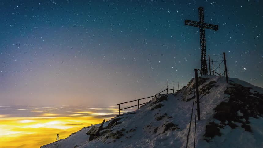 Stars are moving over the mountain summit with a large iron cross on it