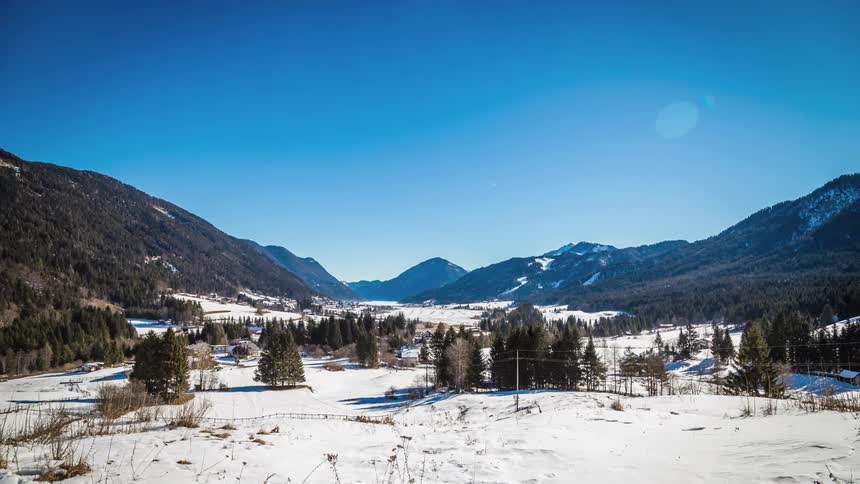A snow covered field between mountains and surrounded by trees