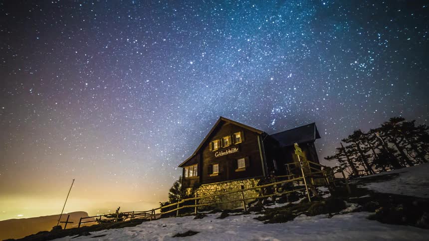 A time lapse of a starry sky above a chalet on a snowy mountain top