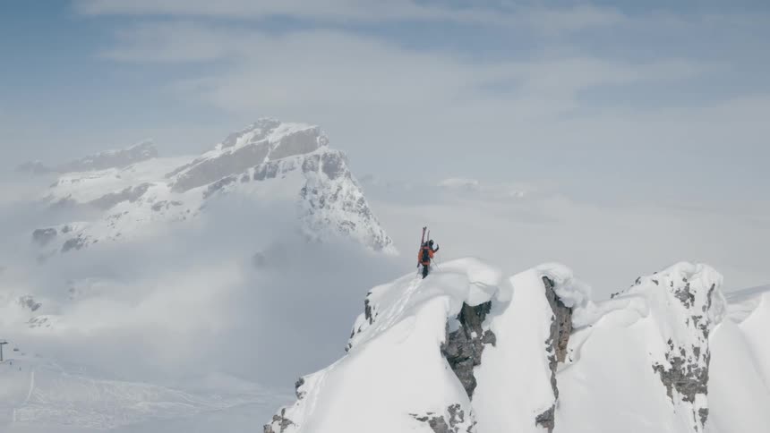 Two people with skis walking on a snowy cliff