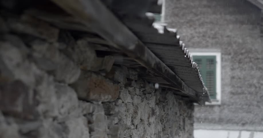 Rain drips off roof on stone house