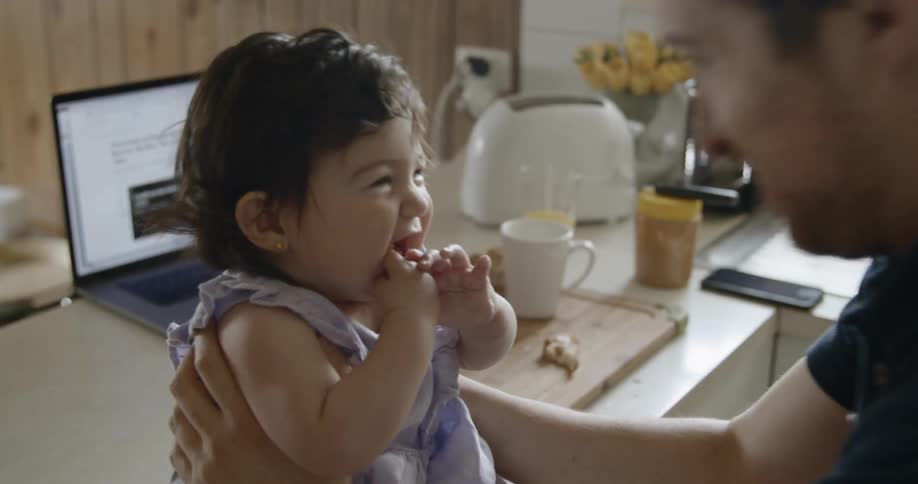 Man holds baby and laugh together in the kitchen during daylight