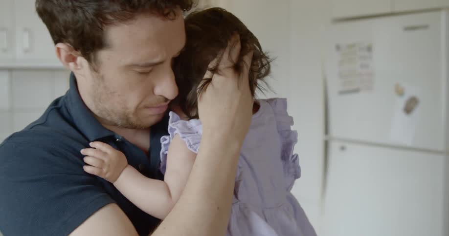 A father holds his infant to his chest and rocks her gently