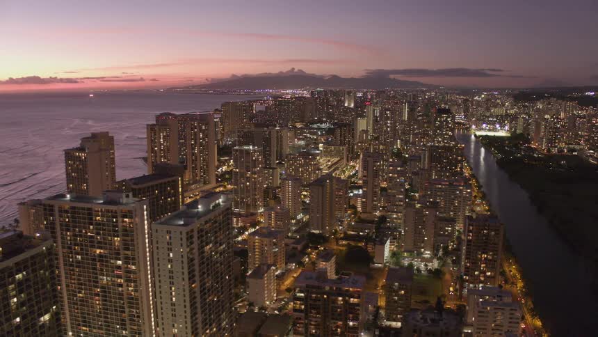 Brightly lit city near ocean at sunset