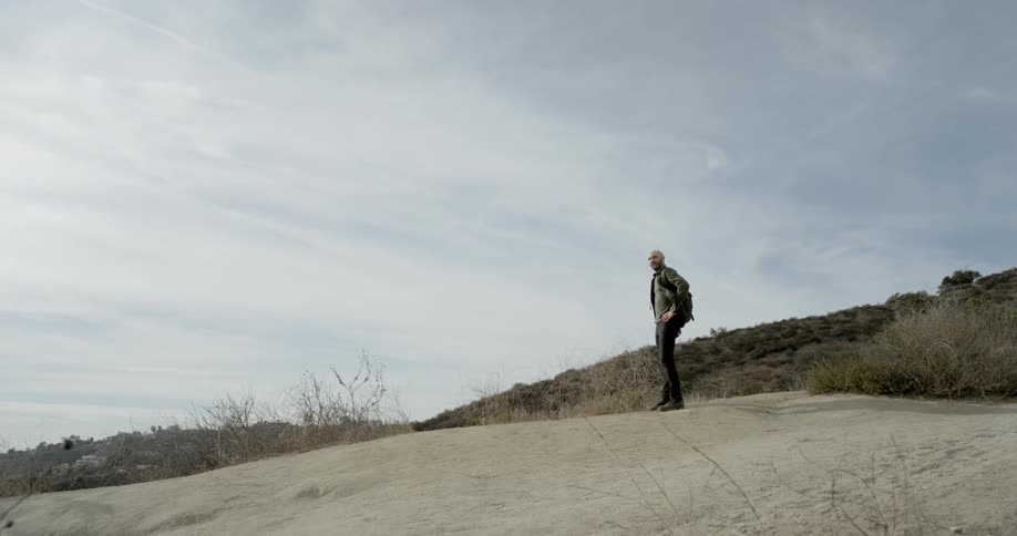 Man with backpack stands on hill looking at the horizon