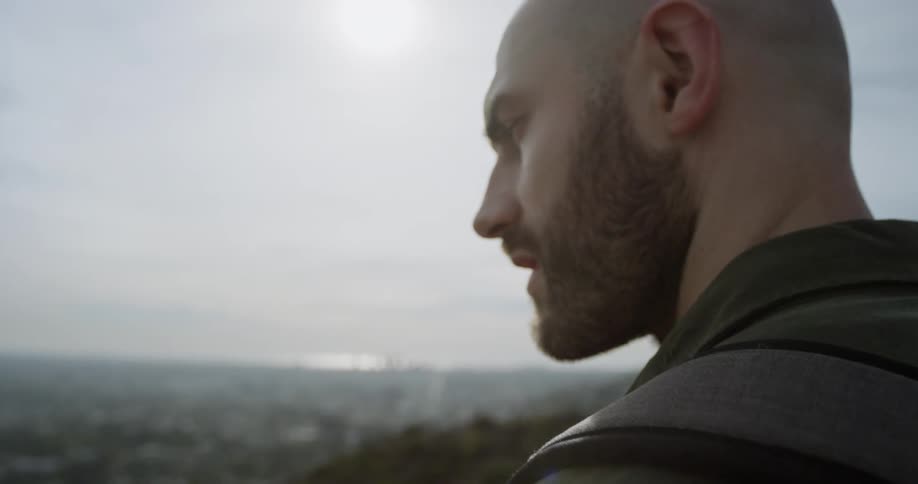 A man stands on top of a hill overlooking a city