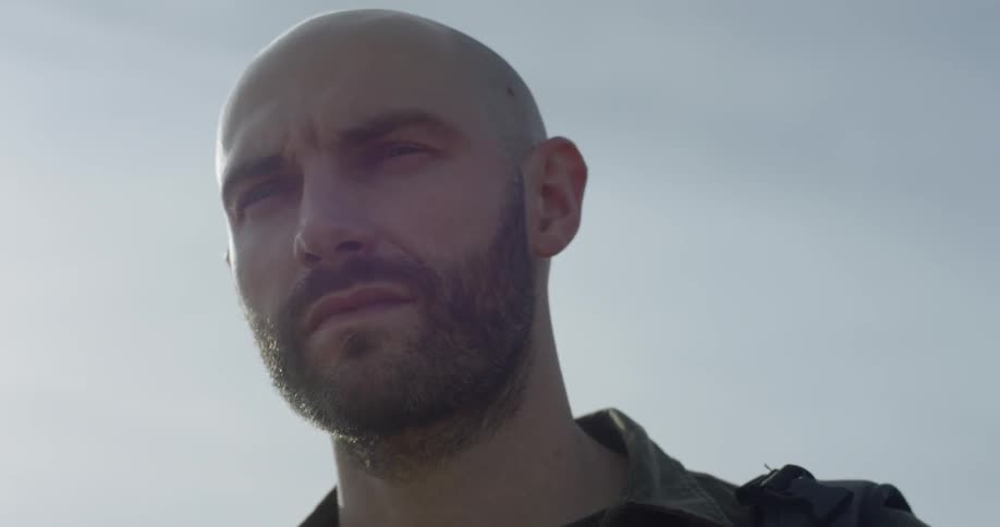 A bald man with a beard man looks around at sunrise
