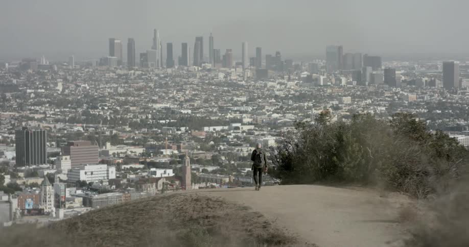 Bald man walks down dirt road hill towards the city during daylight