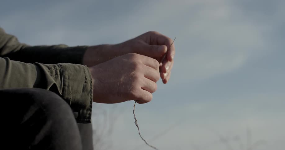 A white man sits outdoors twisting a dead stem