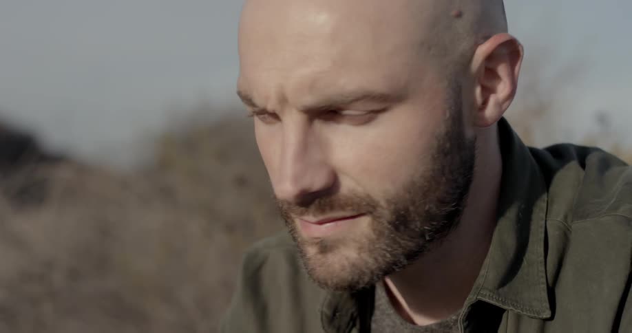 Bearded man sitting outdoors looking at the horizon