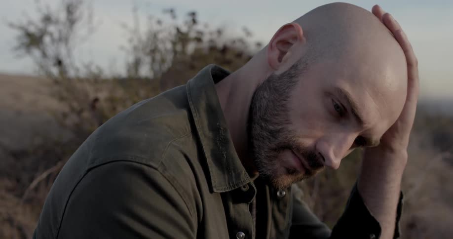 A man is thinking while sitting in a field on a cloudy day