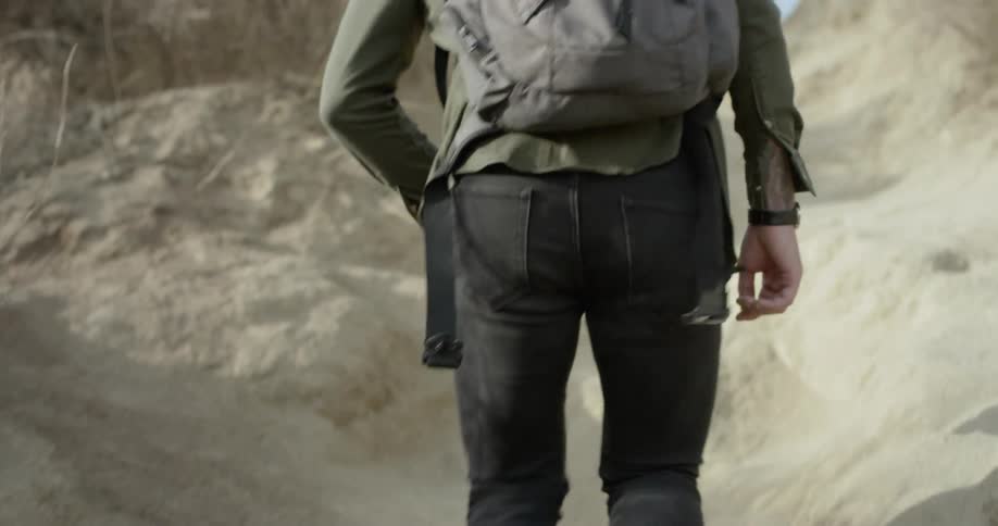 Man walks up sandy hill side carrying backpack