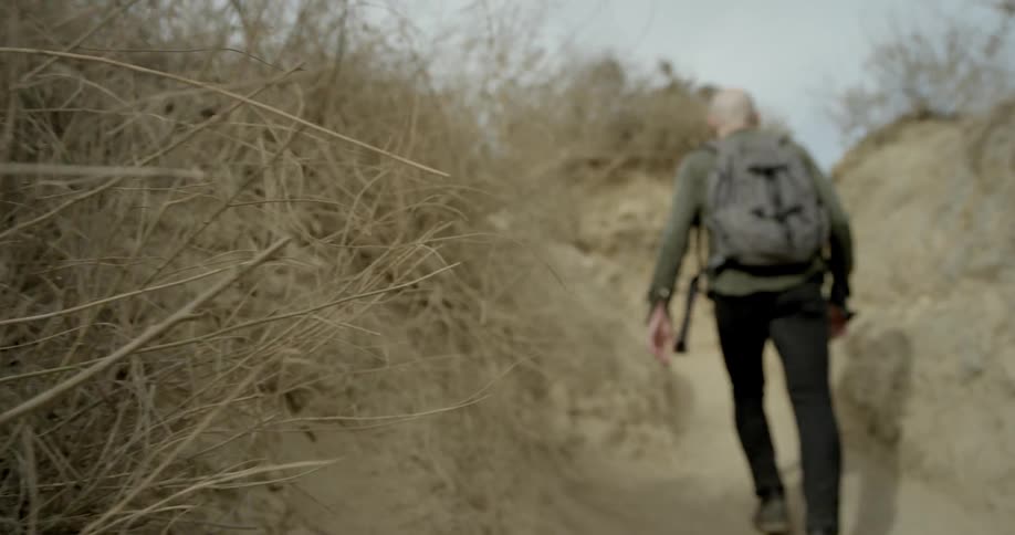 A man hikes up a small dirt hill