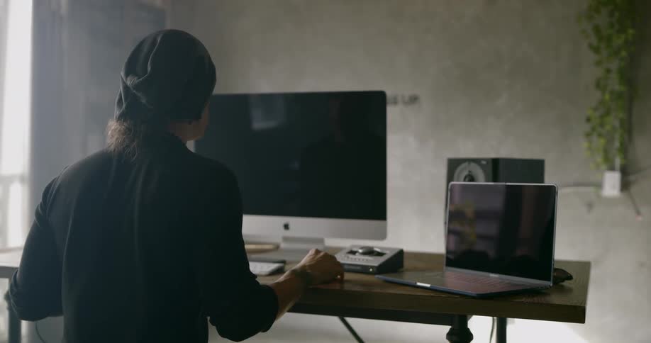 A caucasian man sitting at a wooden desk using an apple computer