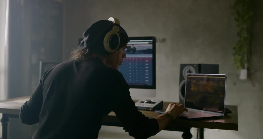 Male wearing headphones editing work on laptop and desktop computer