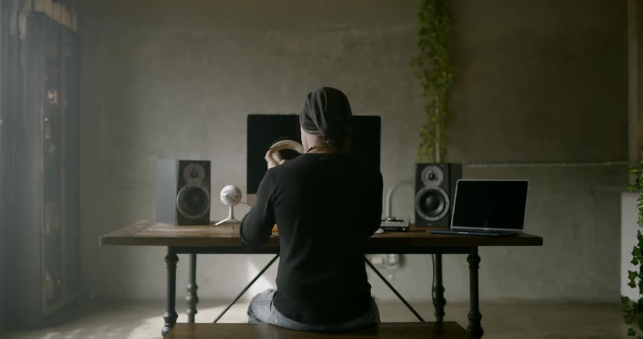 Man sitting at the table wears headphones to listen to music in a room during daylight