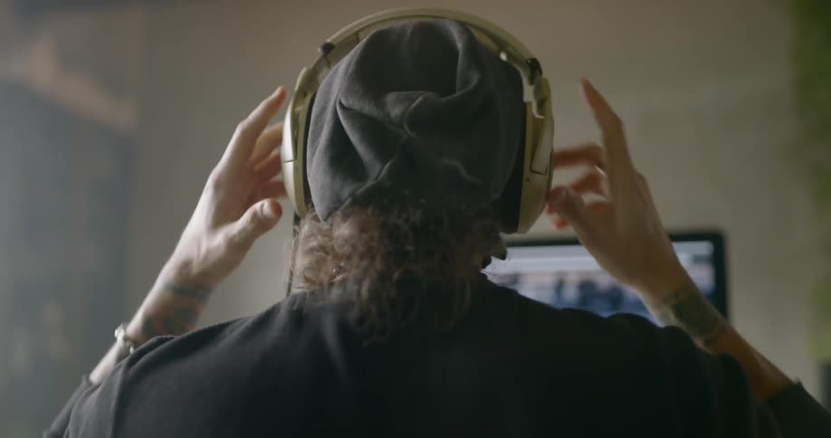 A man sitting before a computer browsing the web and putting on a headset