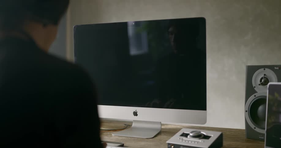A man sits at a desk working on a computer with speakers and wireless keyboard and mouse