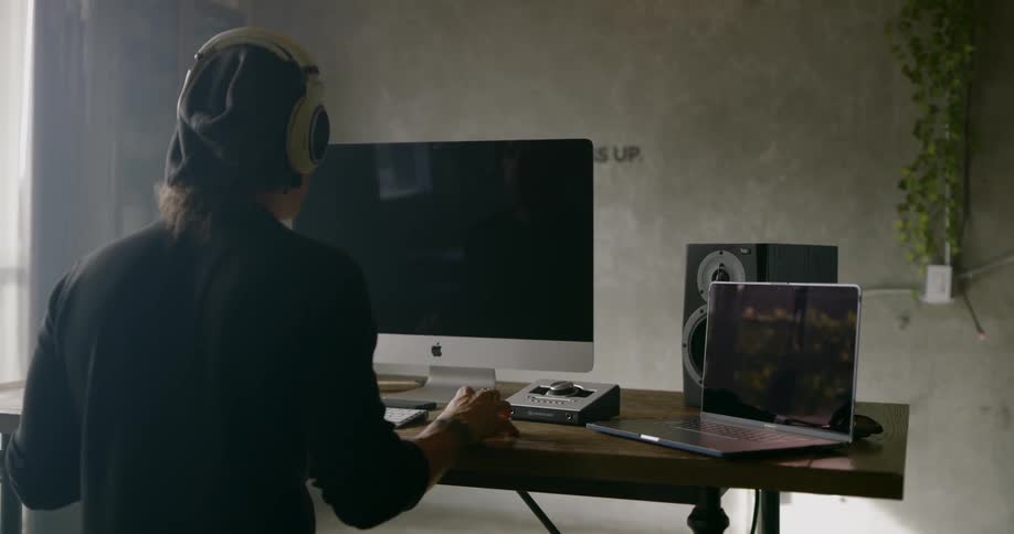 A man wearing a headset sitting at desk using a computer and laptop