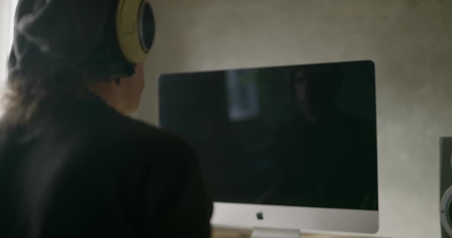 A man sitting in front of a computer puts headphones on