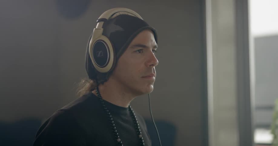 Man by window puts on headphones and nods his head along with what he is hearing