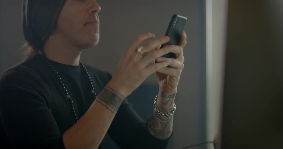 A man sits in front of his computer and uses his cell phone