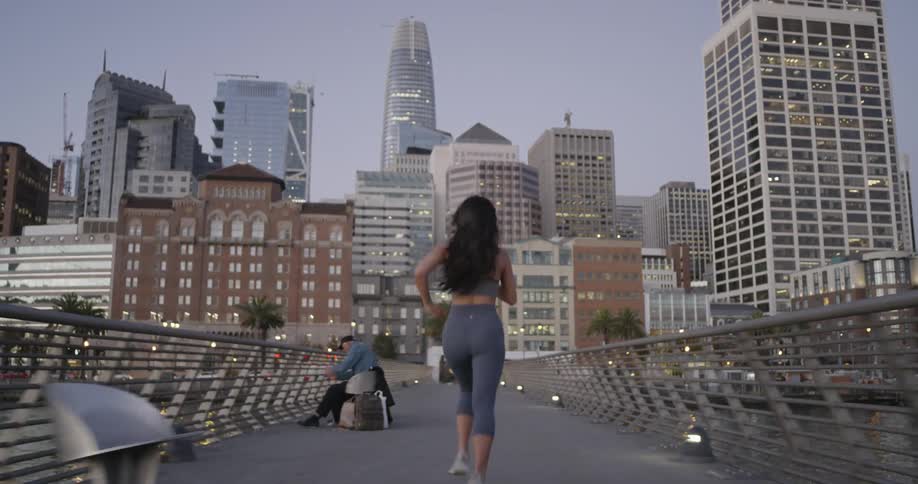 A woman runs over a pedestrian bridge to a large city