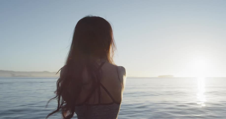 A woman twists and stretches her arms standing on a pier beside the ocean