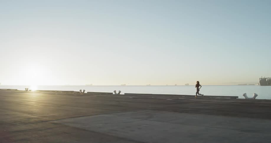 Woman runs along promenade next to the sea while the sun rises