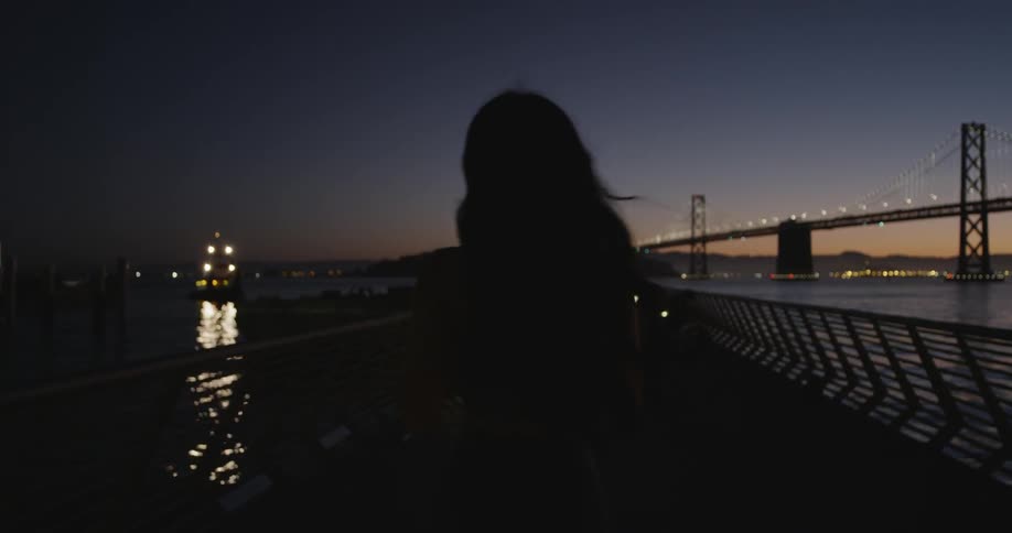 A woman walks down a pier next to a bridge
