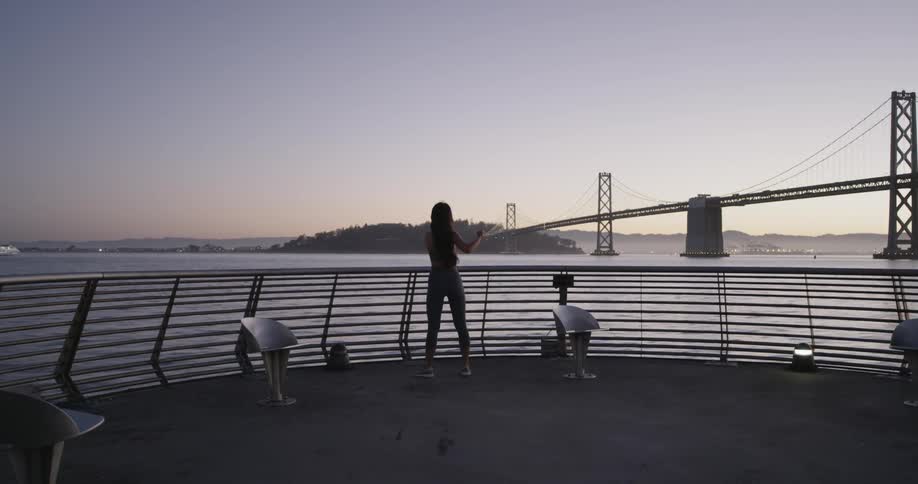 A young woman in workout attire jogs to an observers deck overlooking a bay
