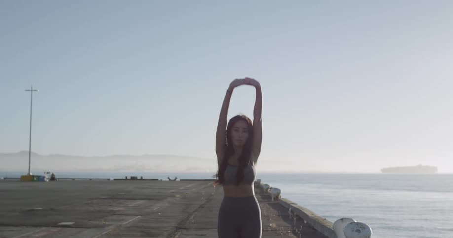 Woman walks along water front stretching then jogs