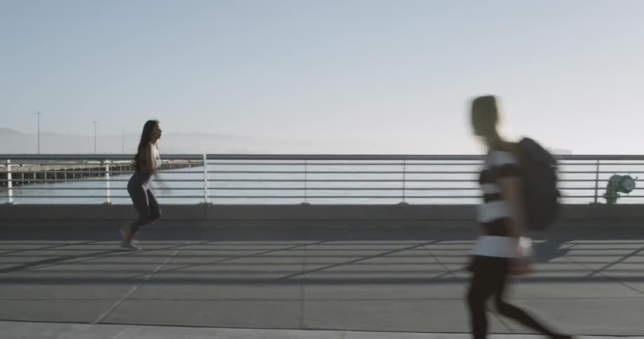 A woman stretches her arms and starts jogging on a waterfront sidewalk