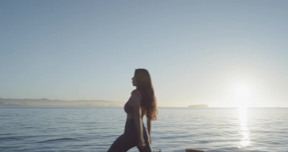A woman stretches her legs and arms standing on a pier