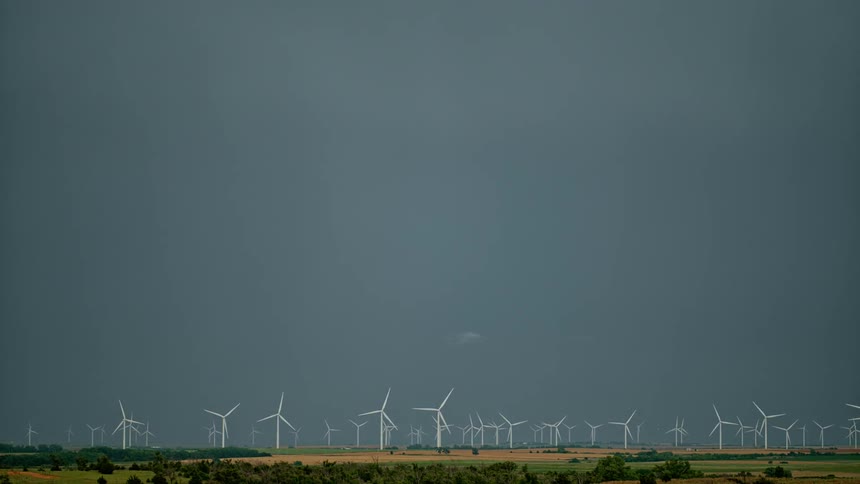 Lightning flashes in the sky above wind turbines in a rural field