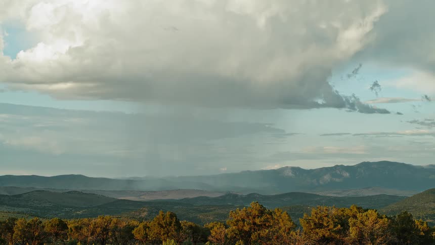 Rain falls from the large white cloud on a grasscovered hills