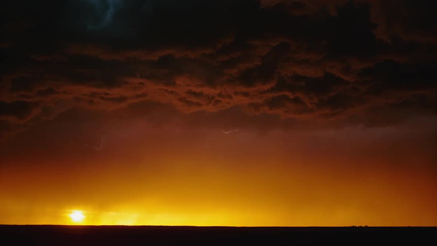 A wide shot of a flat landscape at dusk with storm clouds and lightning