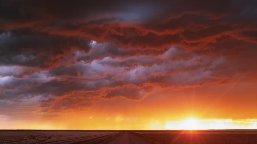 Lightning in clouds over fields and road at sunset