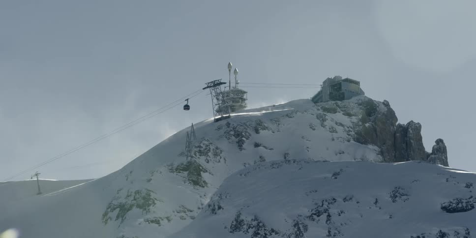 A sky lift moves down the rail beside a snow covered mountain