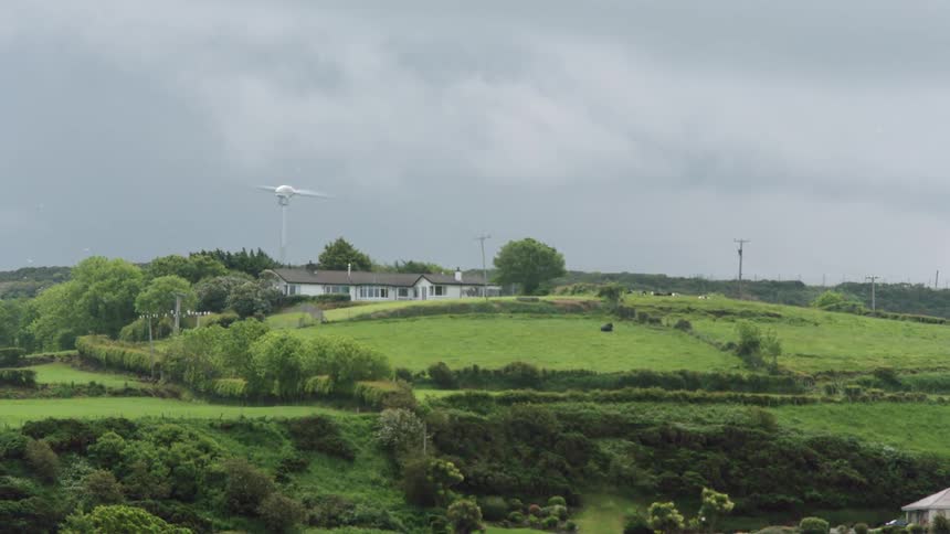 View of a house with a wind power generator built on a grass covered hill