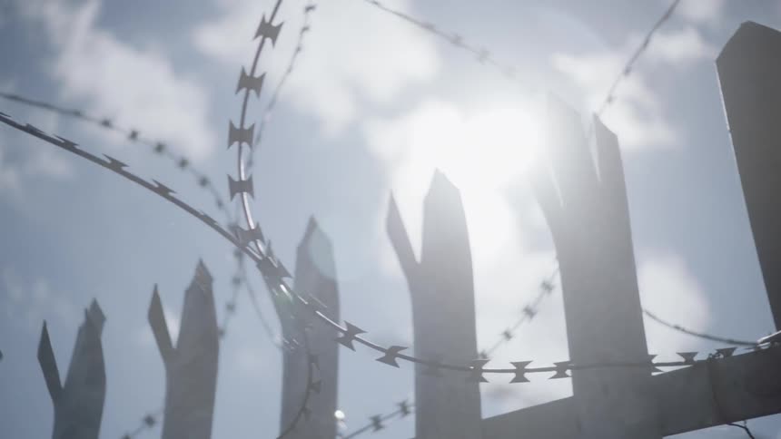 Barbed wire surrounds a pointed broken fence
