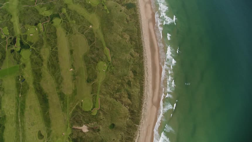 A golf course that juts to the ocean is shown from above