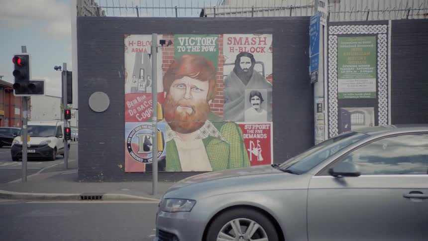 A street corner with a mural on the side of a building as cars pass by in the foreground