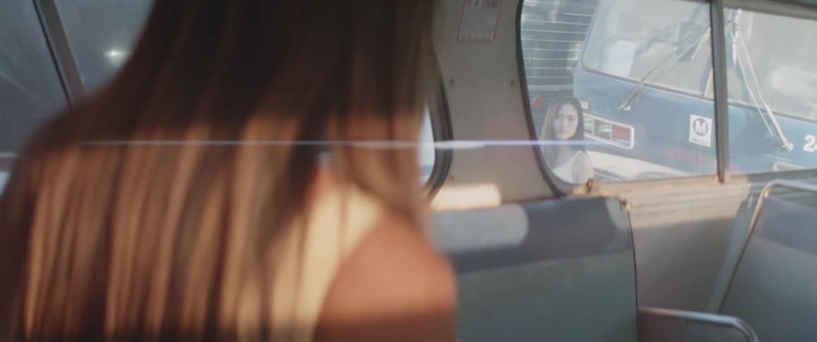 A woman looks out a bus window at another woman
