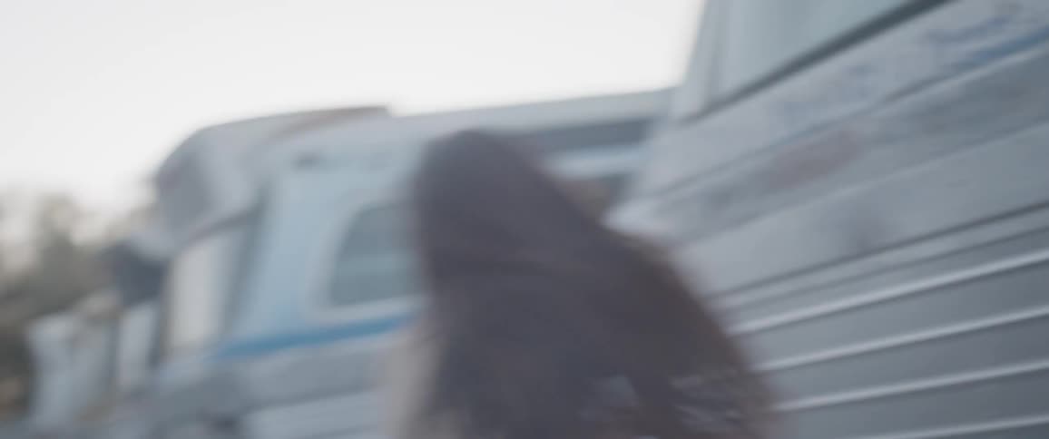 A woman wearing a leotard dances in a lot full of buses