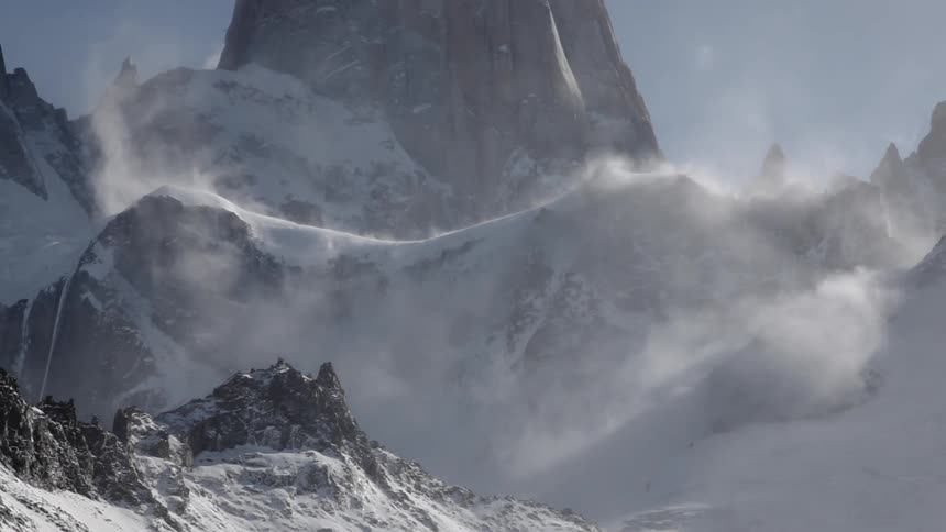 Wind blown snow moves over mountain ridges on a sunny day