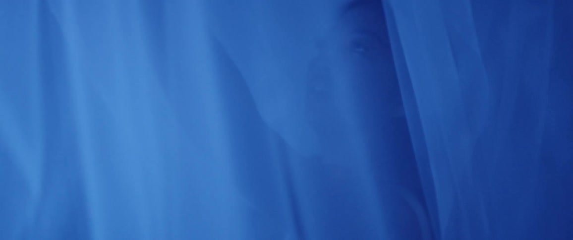 A woman stretches and poses in a tent with veils illuminated by electric blue light