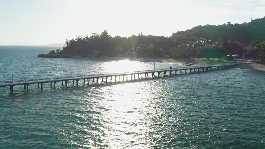 Aerial of a couple walking on a narrow pier on an island at sunset