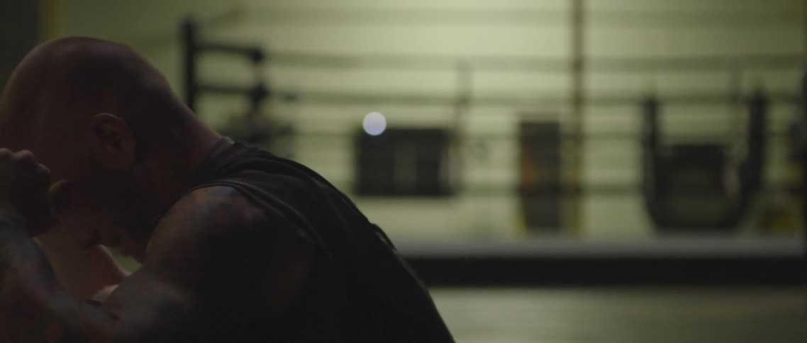 A white male with tattoos is doing sit ups in front of a boxing ring in a gym