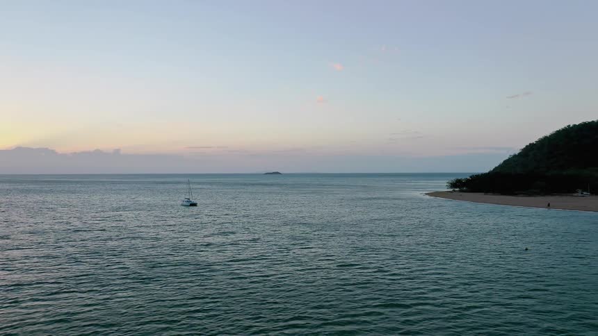 A sailboat off the coast of a sandy beach